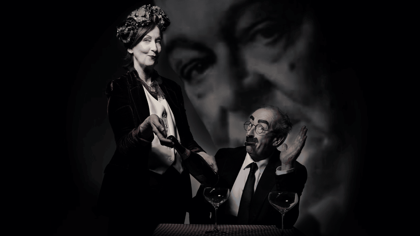 Dinner With Groucho by Frank McGuinness. A waitress is showing a bottle of wine to a seated gentleman. The gentleman is Groucho Marx. In the background, there is a large image of T.S. Eliot