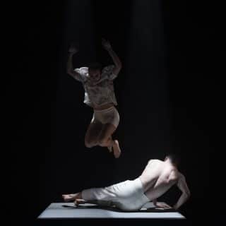 One dancer is jumping mid air above a second dancer who is lying on the floor, attempting to get up. From Brink, 2020, commissioned by Maiden Voyage Dance Company. Photo Credit Luca Truffarelli