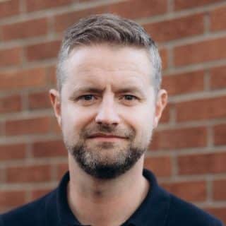 Chris McCreery, AD & CEO of BIAF standing in front of a brick wall.