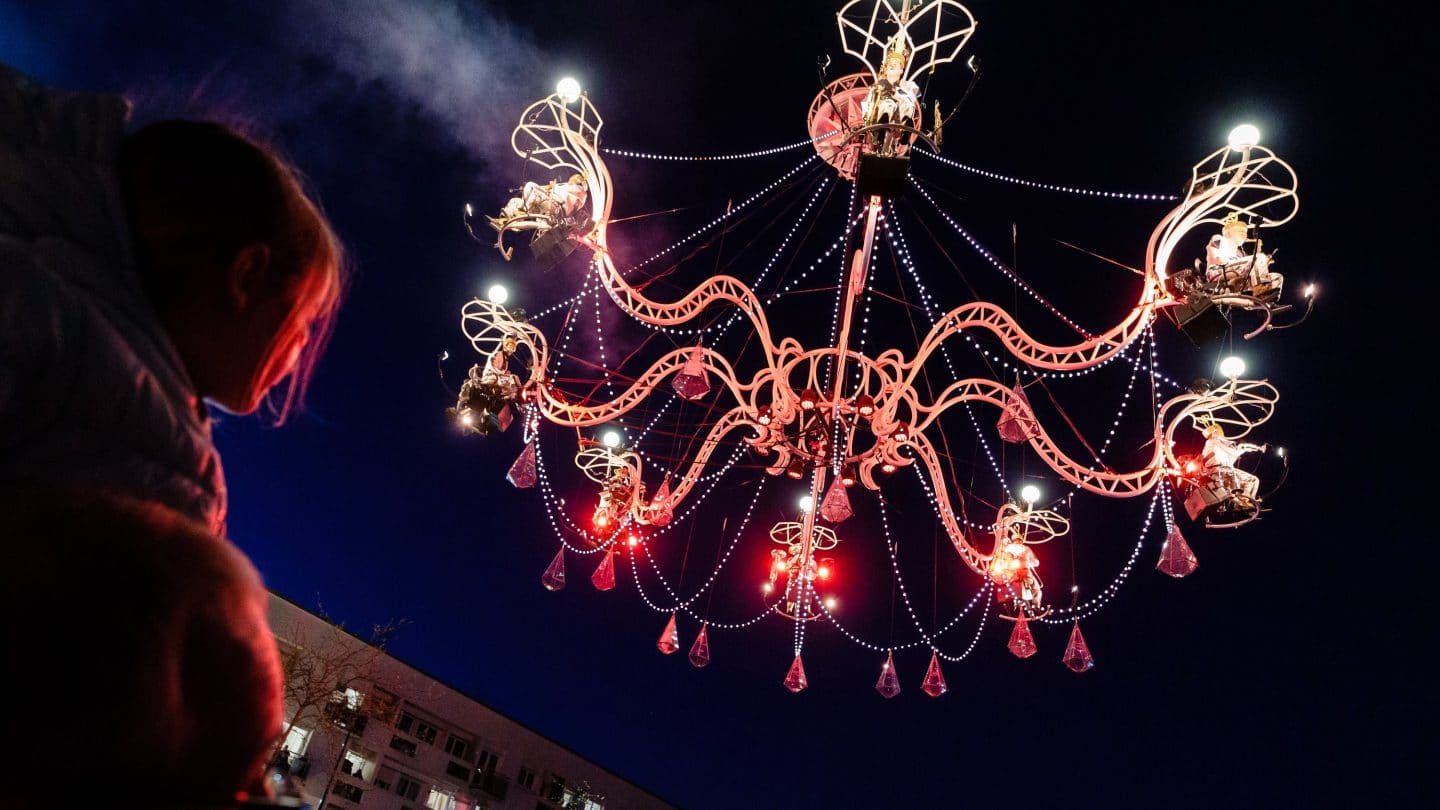 Cristal Palace by Transe Express. Photographer Fred Collier. A young child sits on top of father's shoulders and looks in amazement at gigantic chandelier suspended in the night sky