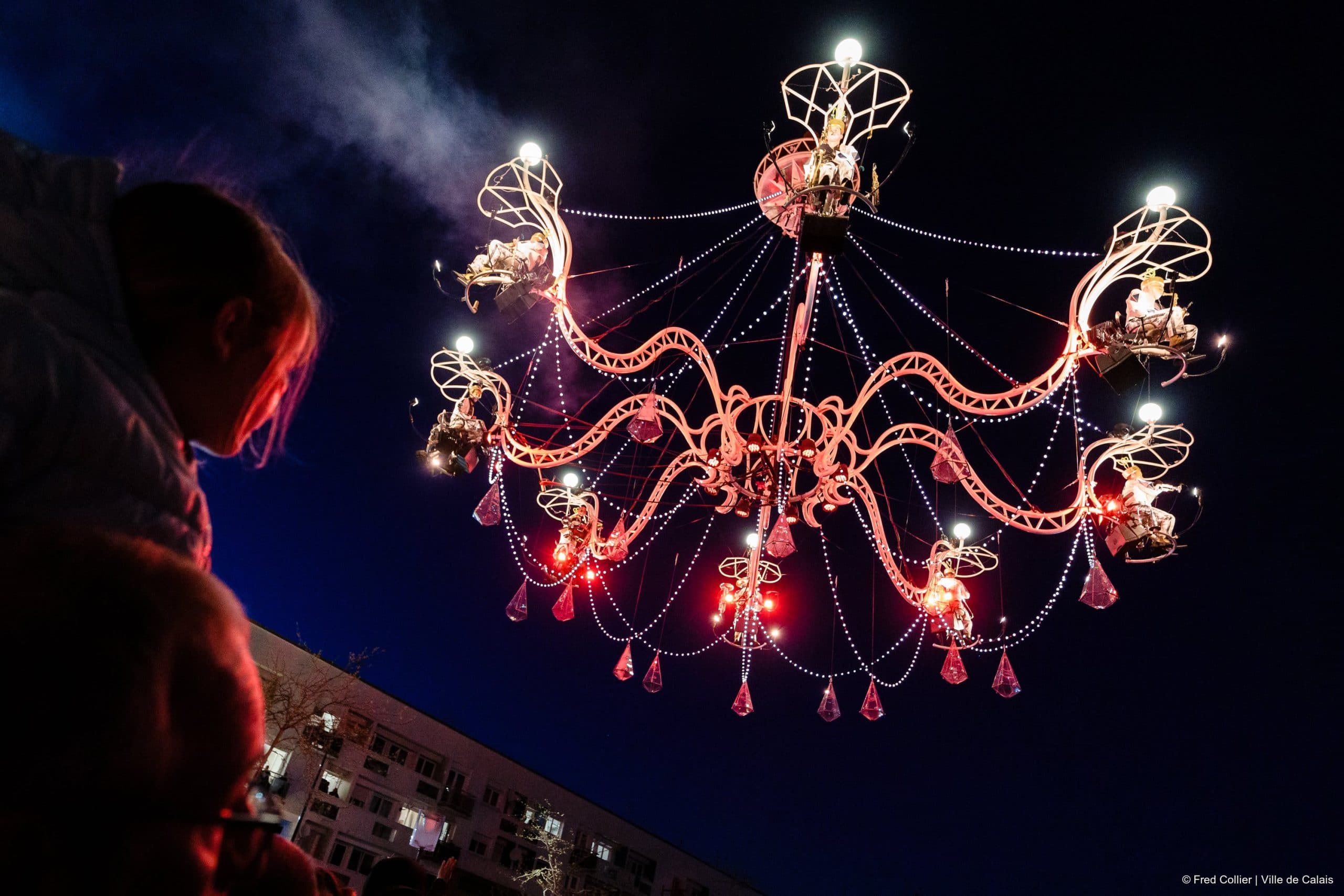 Cristal Palace by Transe Express. Photographer Fred Collier. A young child sits on top of father's shoulders and looks in amazement at gigantic chandelier suspended in the night sky