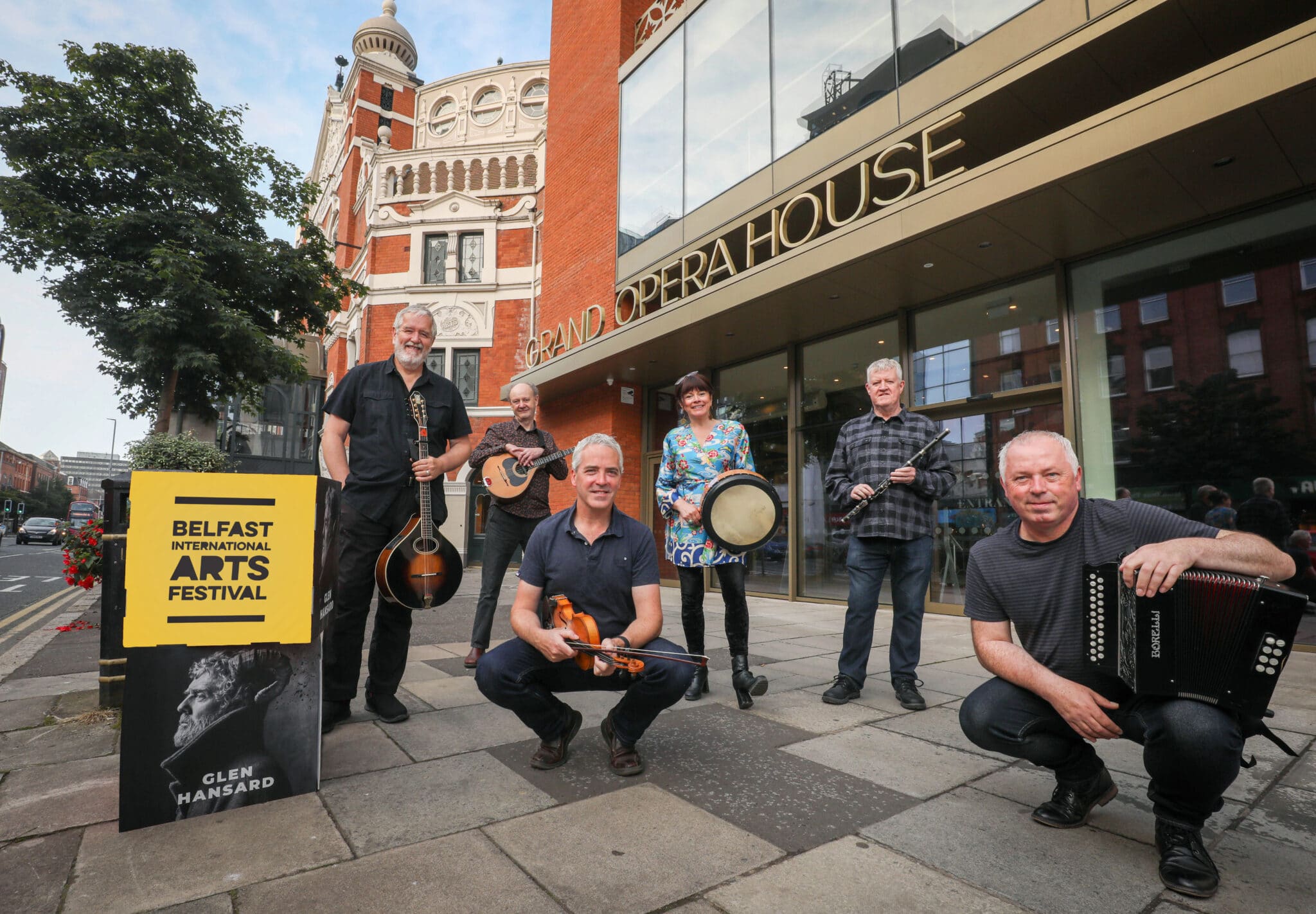 Dervish launch Belfast International Arts Festival 2021 programme. Members of the folk band are posing with their musical instruments outside Grand Opera House, Belfast.