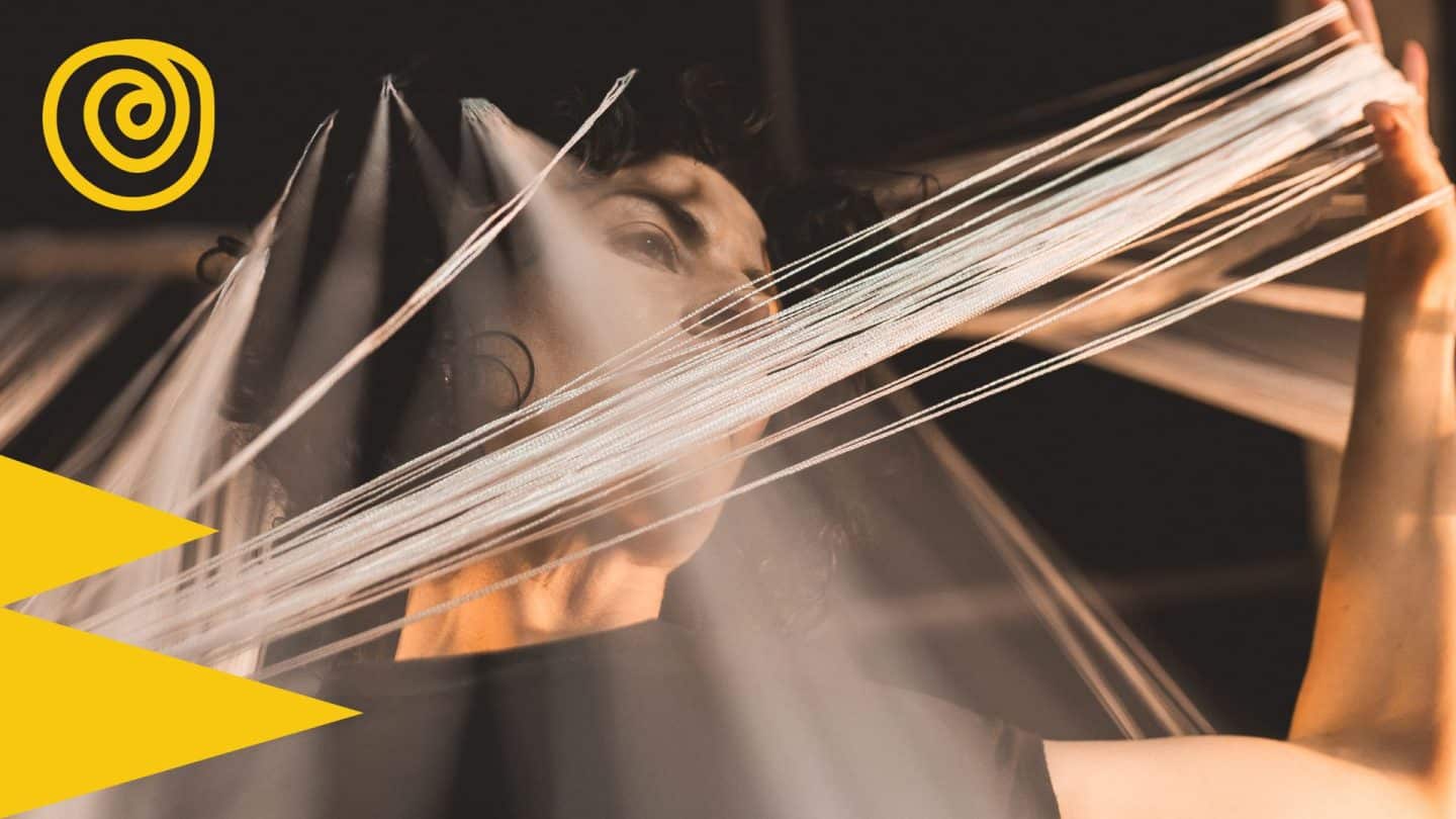 Artist Helen Hall is pictured holding strands of white thread, stretched between her hands.