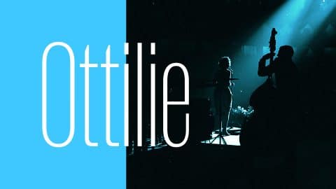Promotional image for “Ottilie.” On the left, the name “Ottilie” appears in large white letters on a bright blue background. On the right, a silhouetted scene shows a live music performance: a woman sings at a microphone while a double bass player stands in the foreground, both illuminated by a dramatic blue stage light.