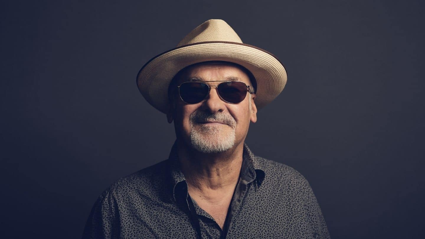 Paul Carrack Photographer Nico Wills. Paul Carrack is wearing a grey shirt, sunglasses and a beige Cuban style straw hat