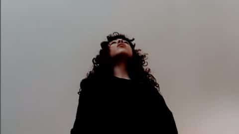 Photo of Salma Ataya. Salma is a young Palestinian woman, she is wearing a black dress and is against a grey background.