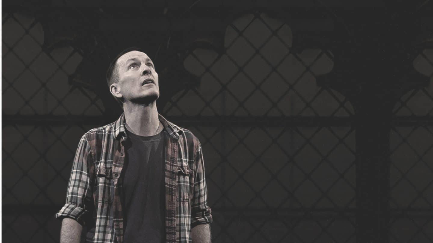 The actor Jay Sefton standing, looking upwards, with a church window in the background.