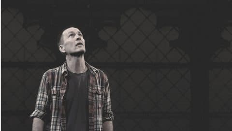 The actor Jay Sefton standing, looking upwards, with a church window in the background.