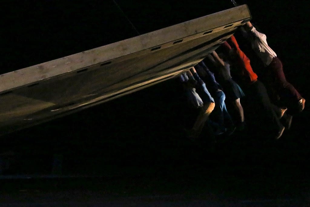 Celui Qui Tombe image of 6 performers hanging onto a moving platform